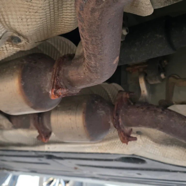 Rusted catalytic converter shown underneath vehicle for catalytic converter buying